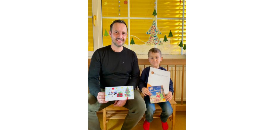 Bürgermeister Luca Fritsch zeigt mit Kind ein gemaltes Bild für die Weihnachtskarten