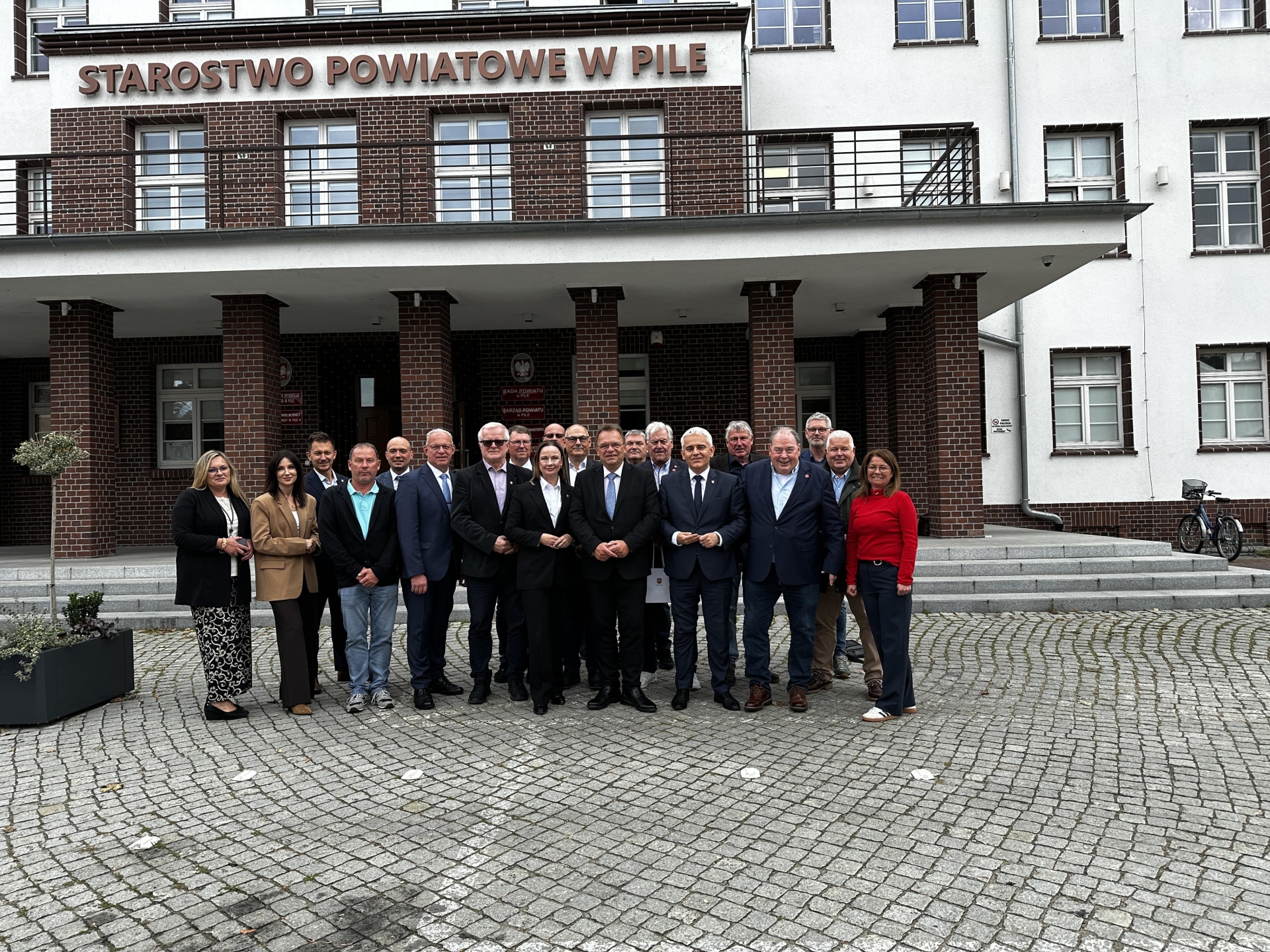 19 Personen vor einem Gebäude in Polen; der Boden besteht aus Pflastersteinen.