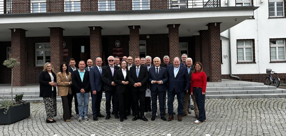 19 Personen vor einem Gebäude in Polen; der Boden besteht aus Pflastersteinen.