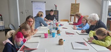 Ulli Becker-Dippel mit Kindern an einem großen Tisch beim Künstlerischen gestalten auf Leinwand in Keilrahmen