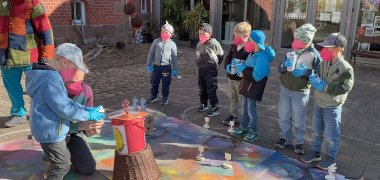  Vor dem Gebäude gestalten Kinder mit Mund-Nasenmaske mit Spray-Farbe gebastelte Blumen