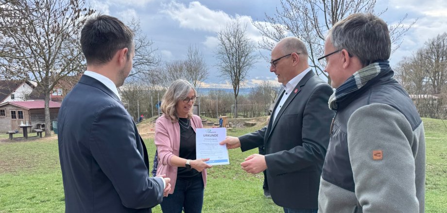 Michaela Wagenführ mit Bürgermeister Luca Fritsch und 2 weiteren Personen bei der Übergabe der Urkunde Klimaschutzpreis des Schwal-Eder-Kreises. Im hintergrund ist der Aussenbereich des Kindergartens zu sehen.