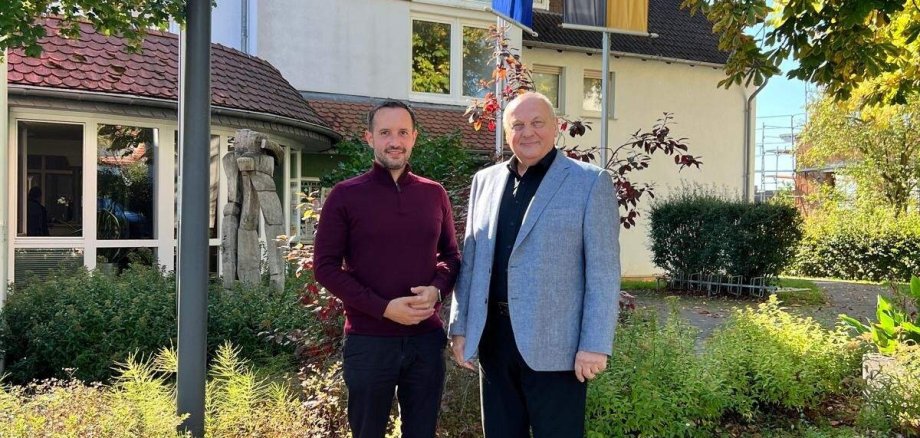 Bürgermeister Luca Fritsch (links) und Dirigent Hans-Reiner Schmidt (rechts) stehen nebeneinander auf dem gepflasterten Vorplatz des Rathauses Willingshausen. Im Hintergrund sind das Rathaus, eine Europaflagge und die Gemeindeflagge zu sehen.